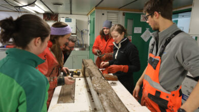 Scientists aboard the Nathaniel B. Palmer examine a newly collected seafloor sediment core from near the front of the Thwaites Glacier ice shelf. Credit Linda Welzenbach